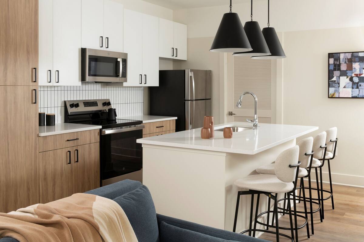 A modern kitchen with white cabinets, stainless steel appliances, and a bar area with stools.