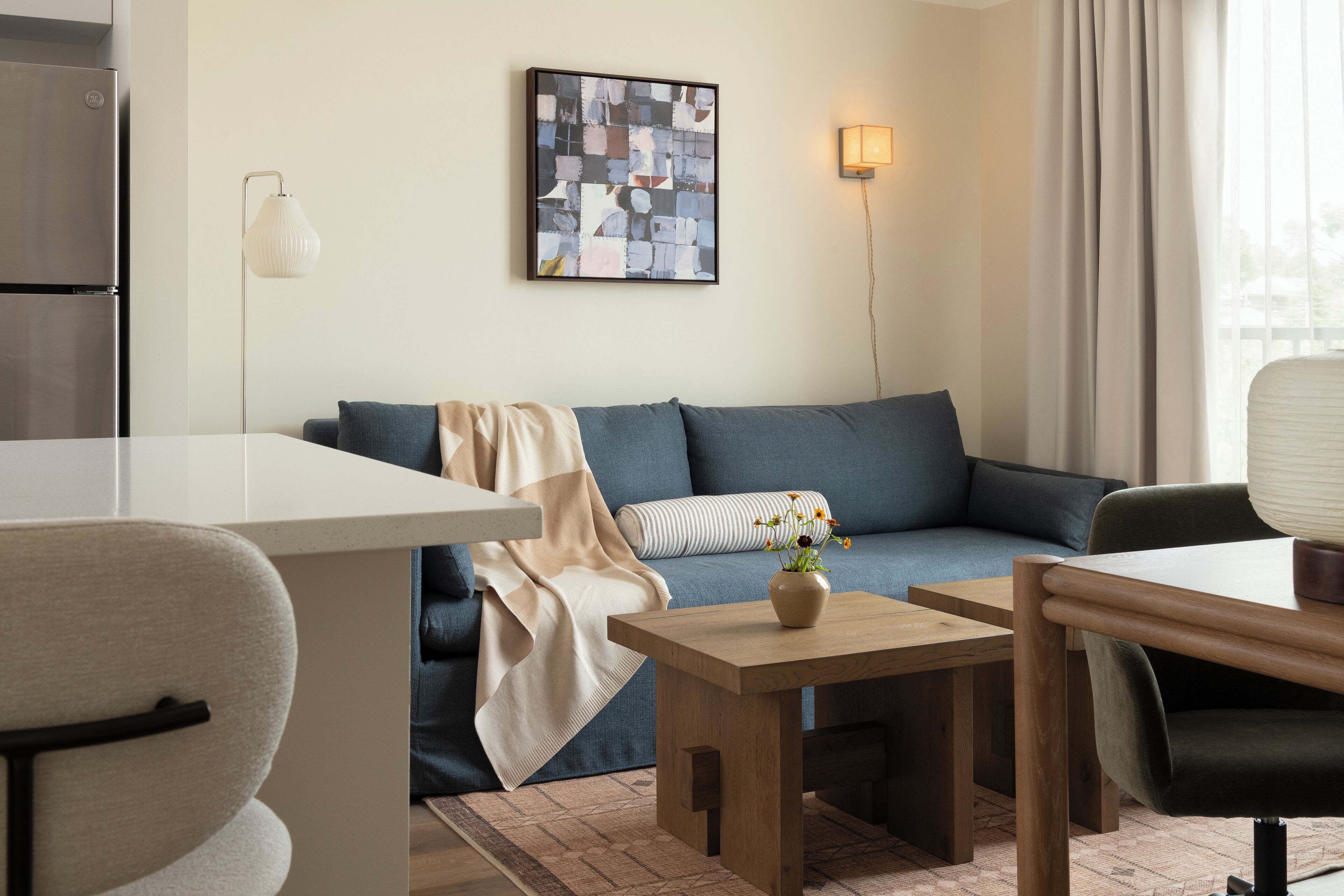 A modern living room with a sofa, a coffee table, a dining table, and a kitchen area with a refrigerator.