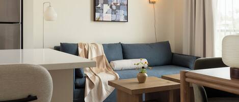 A modern living room with a sofa, a coffee table, a dining table, and a kitchen area with a refrigerator.