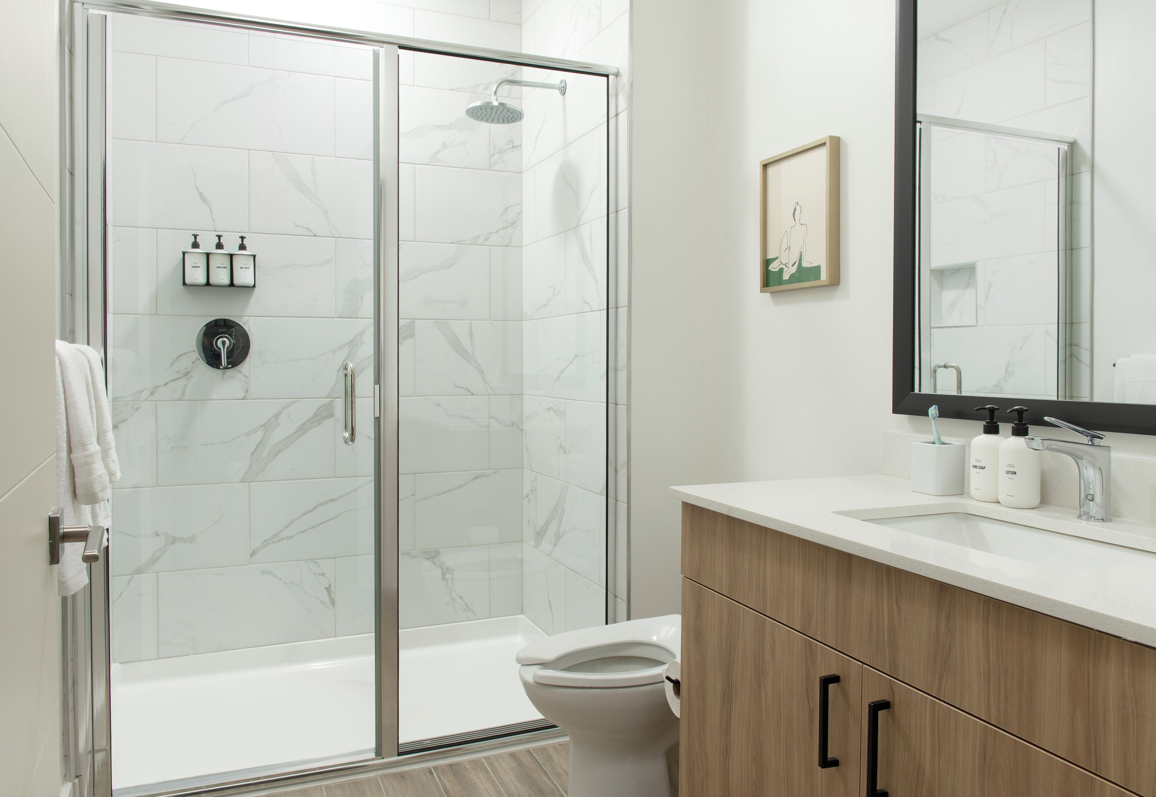 A modern bathroom with a glass-enclosed shower, a white toilet, and a wooden vanity with a mirror.
