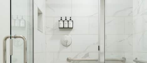 Un área de ducha moderna con puerta de vidrio, cabezal de ducha de mano y panel de control.