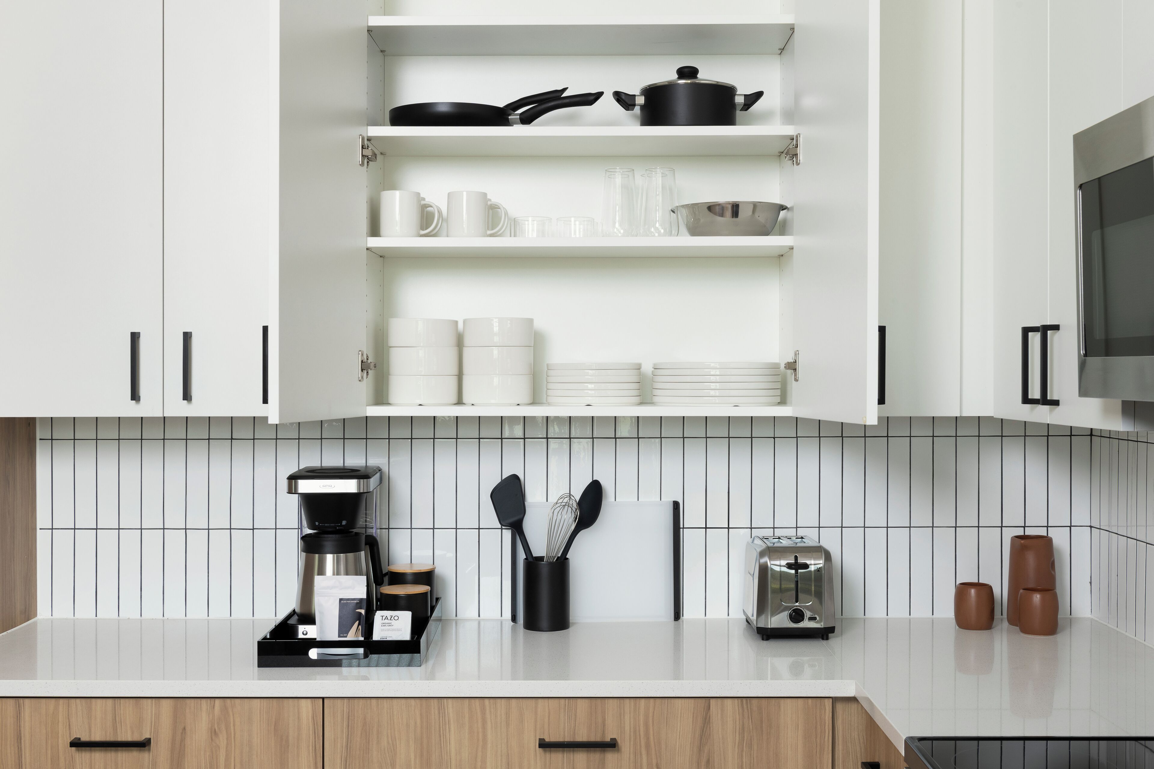 A modern kitchen with white cabinets, a coffee maker, a toaster, and a kettle on the counter.