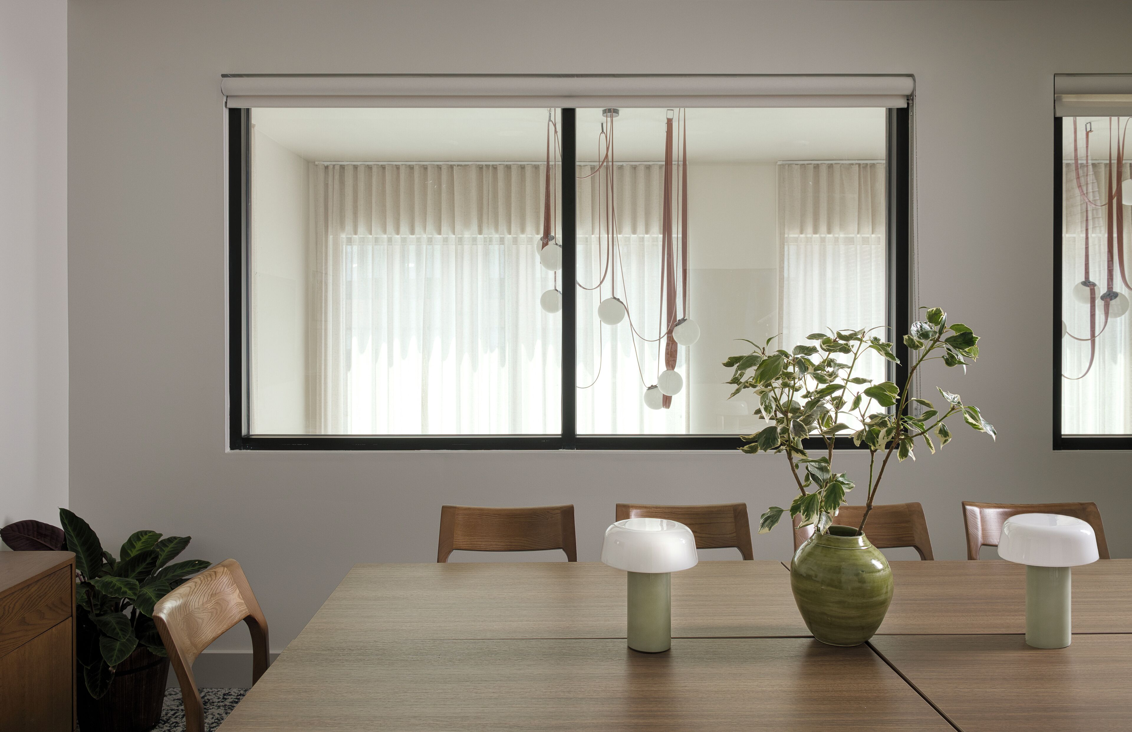 Un comedor con una mesa de madera, sillas, un florero con una planta y una lámpara colgante.