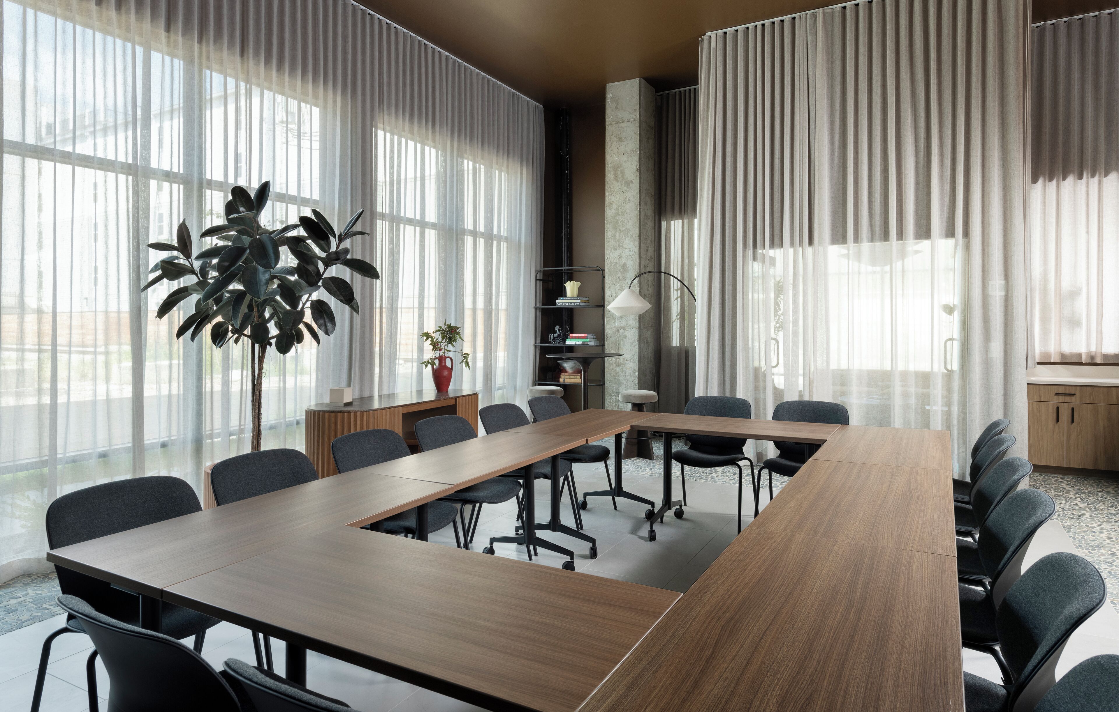 Un salón de conferencias con una larga mesa, sillas, una planta en maceta y una estantería.