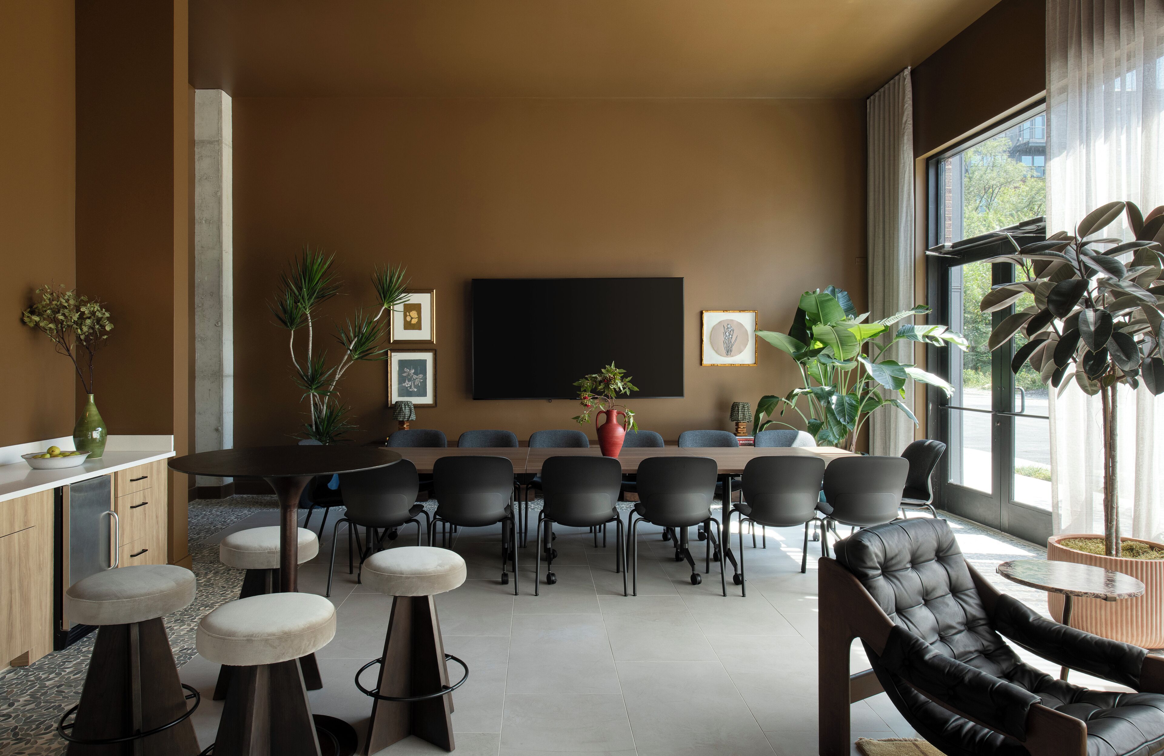 A modern meeting room with a large table, black chairs, and a large window with plants.