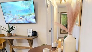 A dining area with a round table, chairs, a television mounted on the wall, and a plant on a side table.