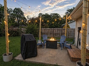 A backyard patio with a grill, chairs, and a fire pit.