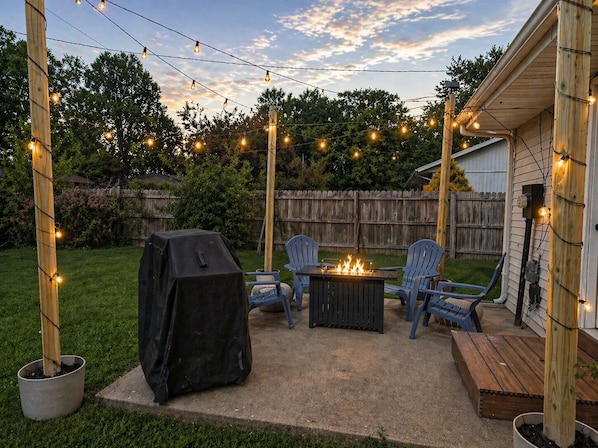 A backyard patio with a grill, chairs, and a fire pit.