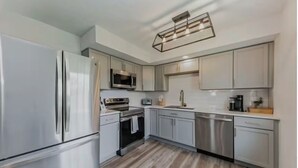 A modern kitchen with stainless steel appliances, light grey cabinets, and a wooden floor.