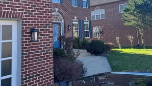A two-story brick house with a garage, a front porch, and a well-maintained lawn. - Lex Holmes Luxury House (Fort Washington)