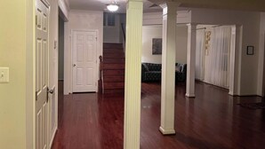 A spacious hallway with wooden flooring, white doors, and a staircase leading to an upper level. - Lex Holmes Luxury House (Fort Washington)