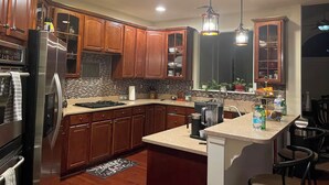 A modern kitchen with wooden cabinets, stainless steel appliances, and pendant lighting. - Lex Holmes Luxury House (Fort Washington)