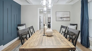 Ein Esszimmer mit einem Holztisch, sechs Stühlen, einer Kristalllüster und einem großen Gemälde an der Wand.
