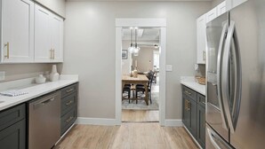 Eine moderne Küche mit weißen Schränken, einem Edelstahlkühlschrank und einem Holzespeisetisch mit Stühlen.
