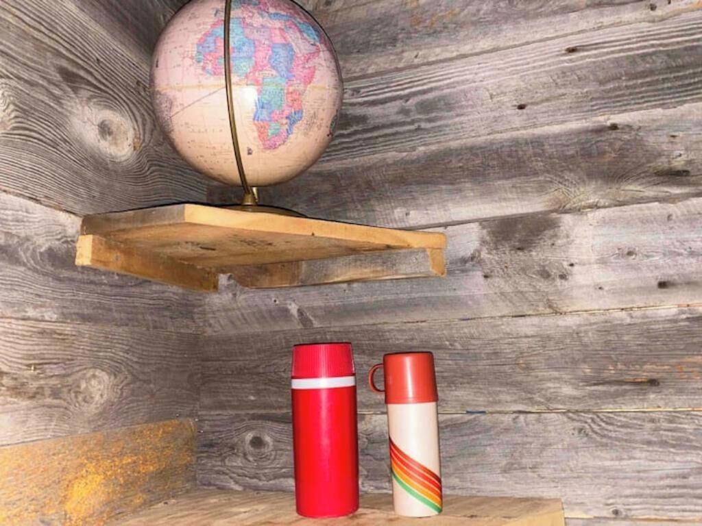 A globe on a wooden shelf, a red thermos, and a white thermos with a rainbow design.