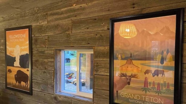 Framed posters of Yellowstone and Grand Teton National Parks on a wooden wall. - West Yellowstone Station At Mountain River Ranch (Ririe)