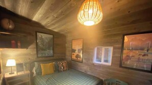 A cozy room with a bed, a chair, a nightstand, and a hanging light fixture. - West Yellowstone Station At Mountain River Ranch (Ririe)