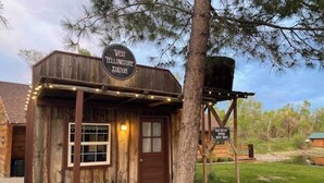 A rustic wooden building labeled "West Yellowstone Station" with a porch and string lights. - West Yellowstone Station At Mountain River Ranch (Ririe)