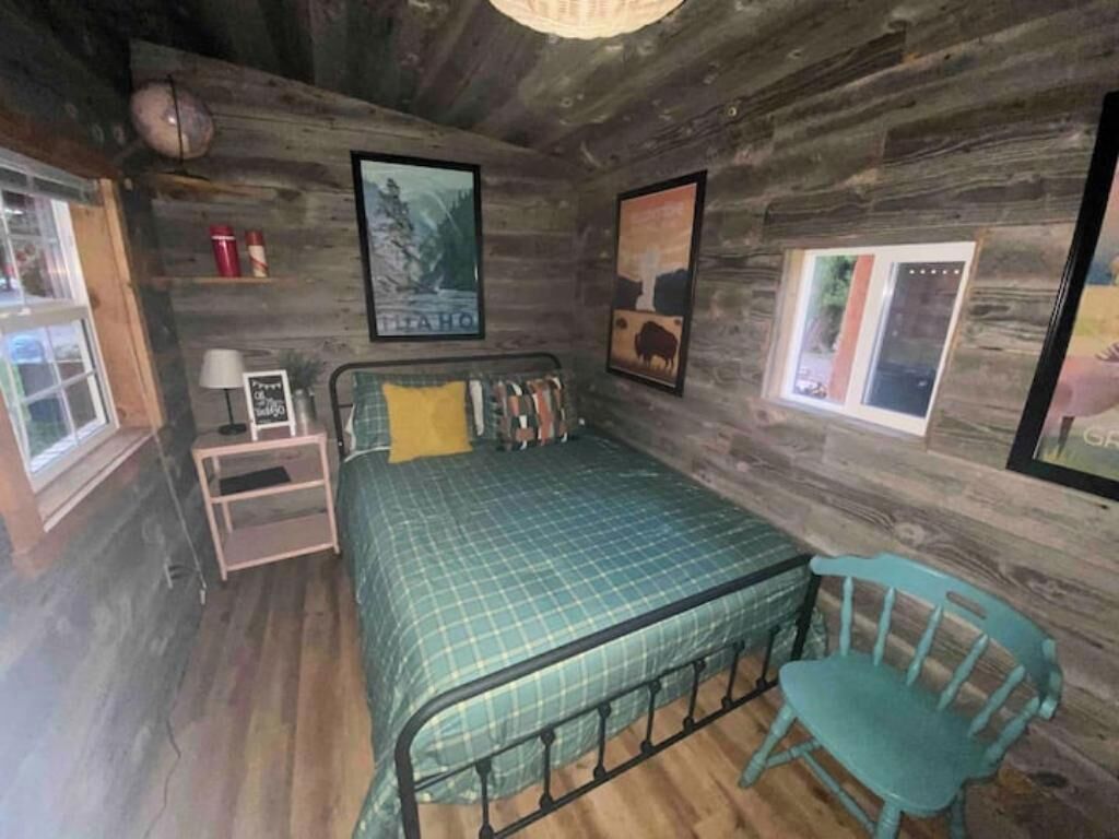 Een houten kamer in rustieke stijl met een bed, een stoel en ingelijste foto’s aan de wanden.