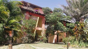 Un edificio de fachada roja y un balcón, rodeado de exuberante vegetación y palmeras.