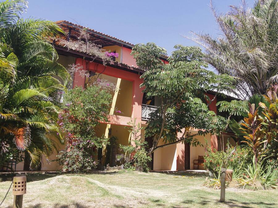 Un edificio de fachada roja y un balcón, rodeado de exuberante vegetación y palmeras.