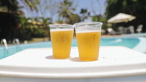 Dos vasos de plástico con una bebida sobre una superficie blanca junto a una piscina.