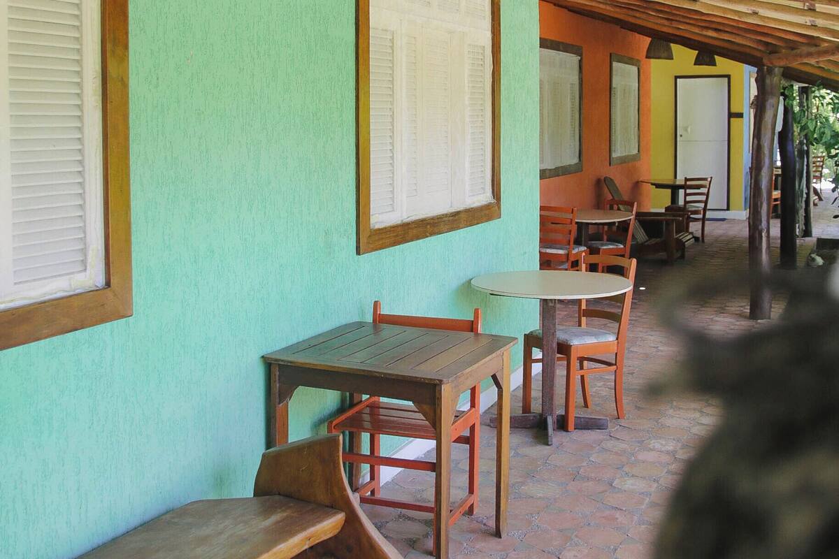 A covered outdoor seating area with wooden tables and benches, a tiled floor, and a green wall with framed pictures.