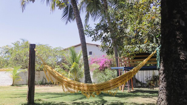 A hammock in a grassy area with trees and a building in the background.