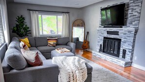 A modern living room with a grey sofa, a fireplace, a television, and a guitar.