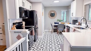 A modern kitchen with white cabinets, a black refrigerator, a microwave, and a dining area with a patterned floor.