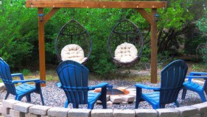 A wooden pergola with two hanging chairs and a fire pit.