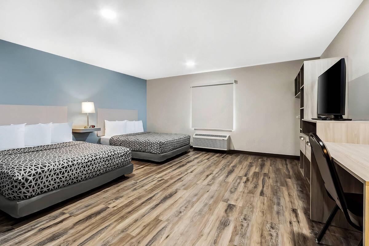 A hotel room with two beds, a desk, a TV, and a window.