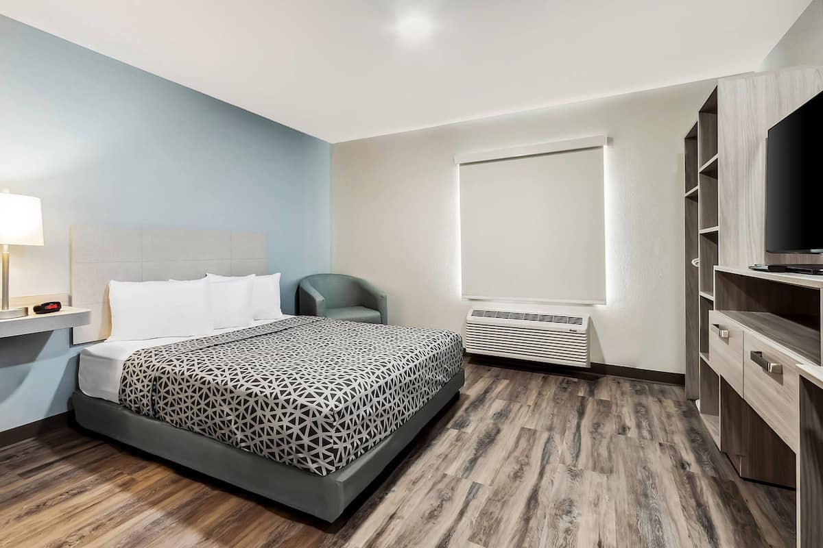 A modern hotel room with a large bed, a TV, a desk, and a window.