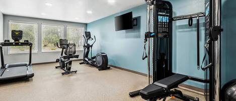 Ein Fitnessstudio mit Laufbändern, Crosstrainern, einem stationären Fahrrad und einem Squat-Gestell.
