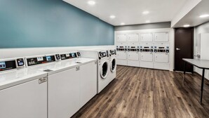 Un moderno cuarto de lavandería con varias lavadoras y secadoras, suelo de madera y una pared azul decorativa.