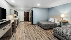 Una habitación de hotel con kitchenette, dos camas, televisor y escritorio.