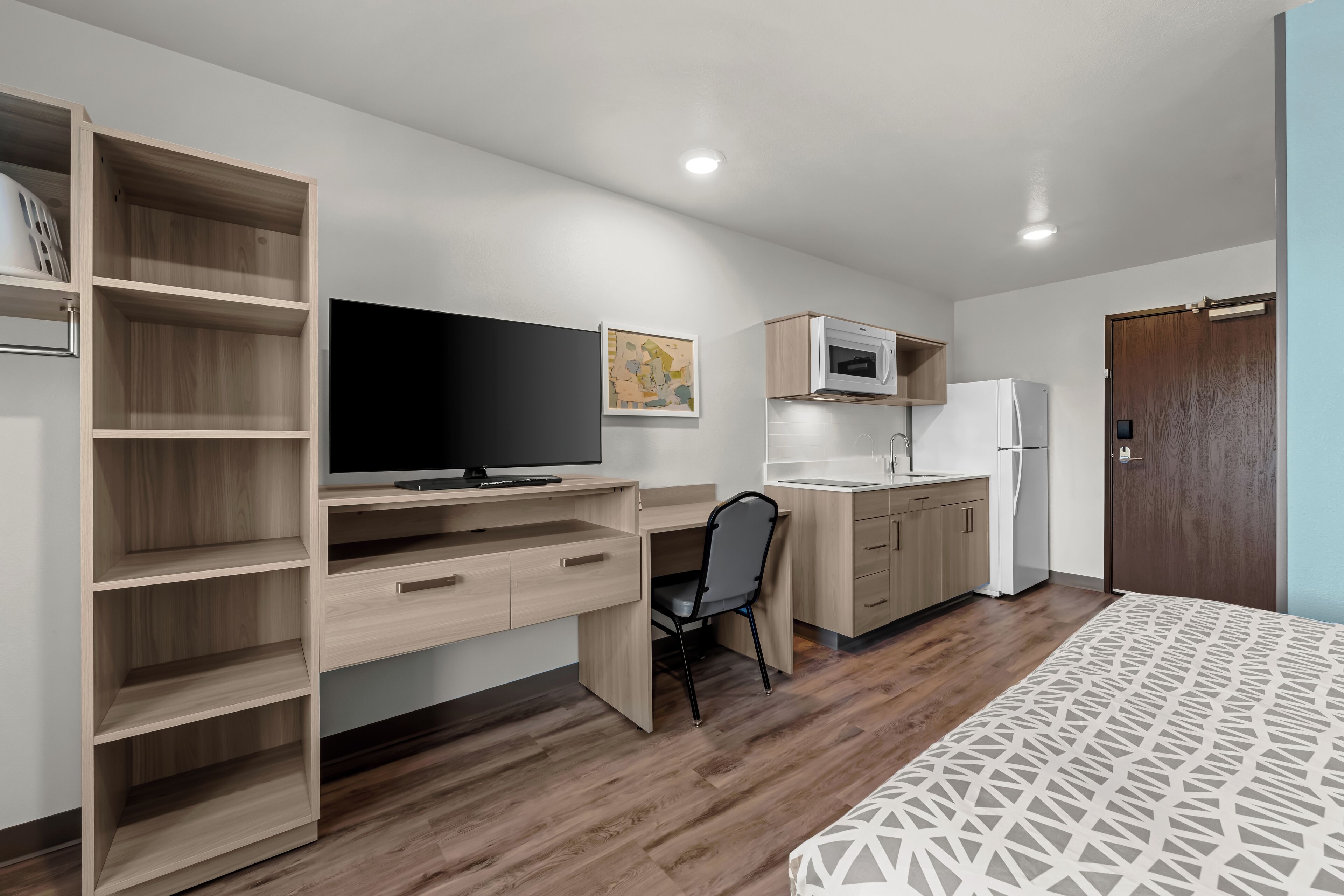 Ein kleines Zimmer mit einem Holzbüro, einem Sessel, einem Fernseher, einer Mikrowelle und einem Kühlschrank.