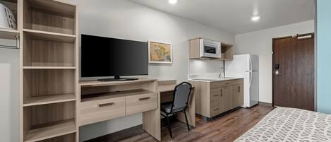 Ein kleines Zimmer mit einem Holzbüro, einem Sessel, einem Fernseher, einer Mikrowelle und einem Kühlschrank.