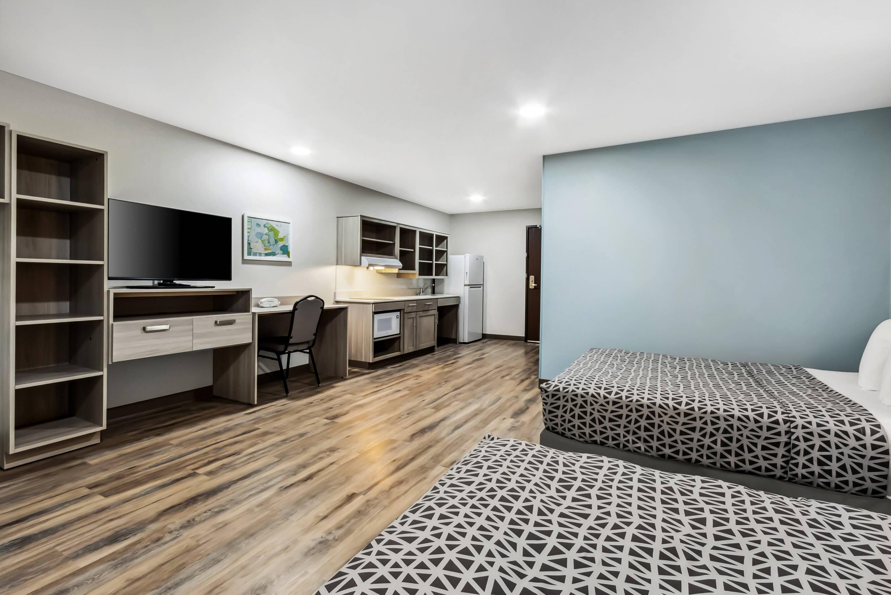 A modern bedroom with a desk, chair, and a TV. There are two beds with patterned bedding.