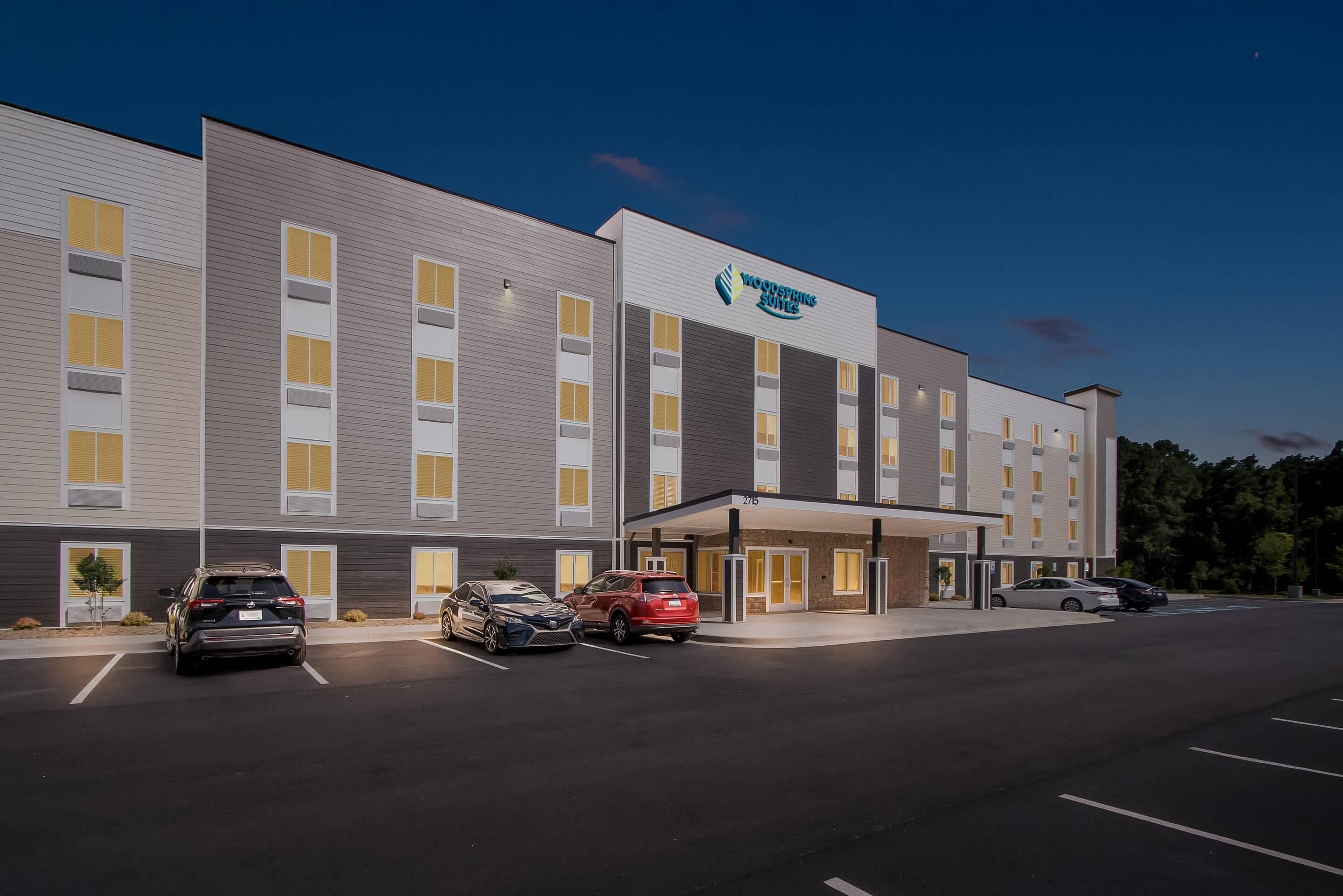 Un hotel moderno con entrada cubierta, varios espacios de estacionamiento y fachada bien iluminada.