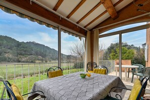 A covered patio with a table set for two, overlooking a grassy field and hills.