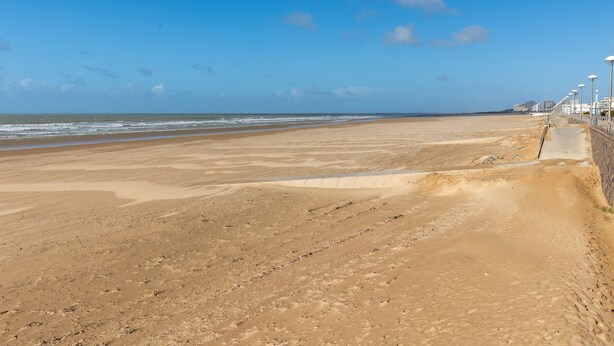 Ein weiter, sandiger Strand mit klarem Himmel und vereinzelten Wolken.