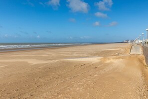 Een breed zandstrand met een heldere lucht en enkele wolken.