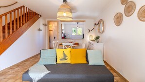 Ein gemütliches Schlafzimmer mit einer Holztreppe, einem Bett mit bunten Kissen, einer gewobenen Deckenleuchte und einem Essbereich im Hintergrund.