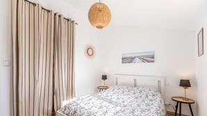 Ein Schlafzimmer mit einem Bett, zwei Nachttischen mit Lampen, einer Pendelleuchte, einem Wandbild und einem Vorhang mit vertikalen Streifen.