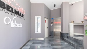 Un pasillo moderno con suelo y paredes grises, un mostrador de recepción y una escalera que lleva a un ascensor.
