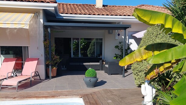 A swimming pool with a wooden deck, lounge chairs, and potted plants. - Charming house with pool and garden, 10 minutes from the sea (Biscarrosse)