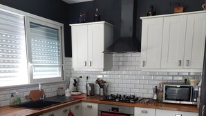 A modern kitchen with white cabinets, a black backsplash, and a wooden countertop. There is a bowl of fruit on the counter, a microwave, and a stove. - Charming house with pool and garden, 10 minutes from the sea (Biscarrosse)