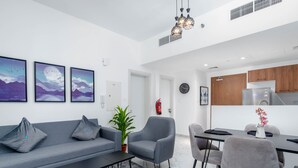 A modern living room with a grey sofa, armchairs, a coffee table, and a dining area with a table and chairs. There are three framed pictures on the wall, a potted plant, and a fire extinguisher. - Bloomfields Executive 1BR Oasis Masdar (Abu Dhabi)