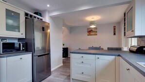 Een moderne keuken met een roestvrijstalen koelkast, een inbouwmagnetron en grijze aanrechtbladen.